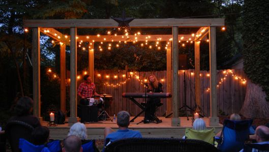 a group of people sitting in chairs on top of a wooden deck with string lights