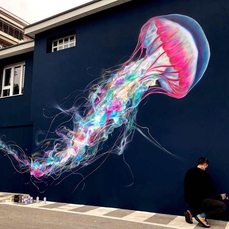 a person sitting on the ground in front of a wall with a jellyfish painted on it