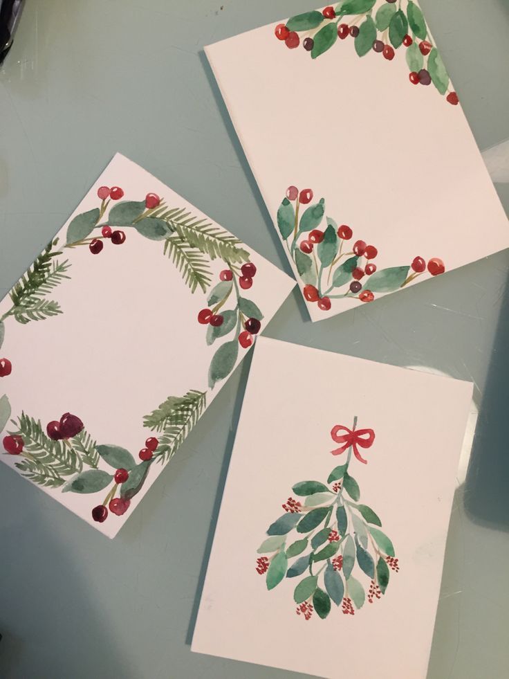 three cards with holly and berries on them are sitting on a table next to scissors