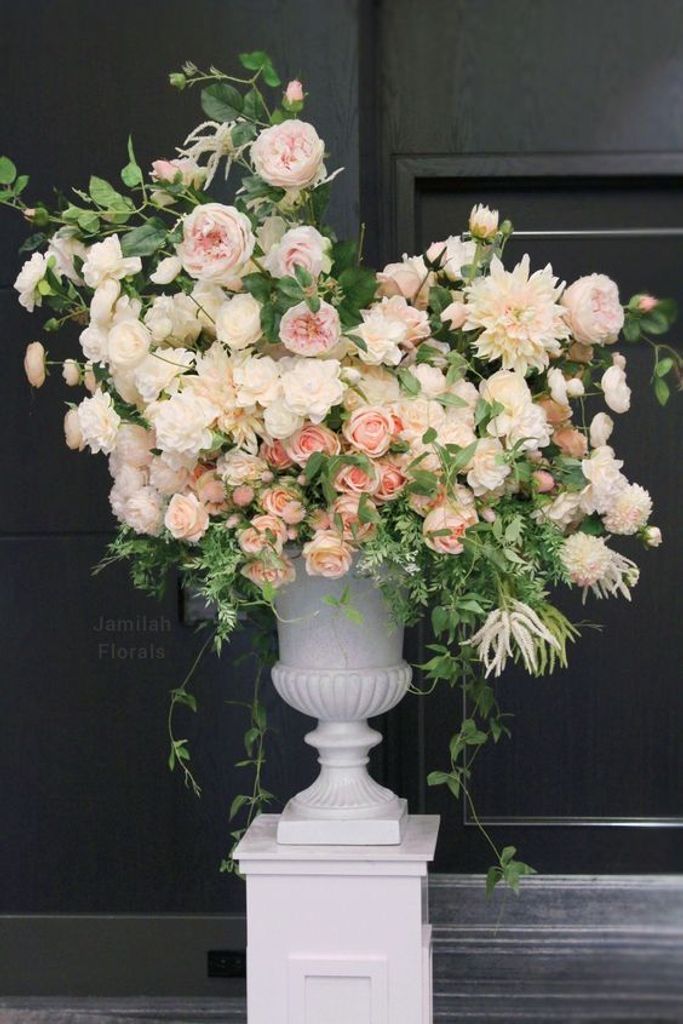 a large white vase filled with lots of flowers on top of a wooden floor next to a black door