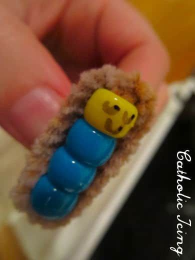 a hand holding a tiny toy in the shape of a caterpillar with yellow and blue eyes