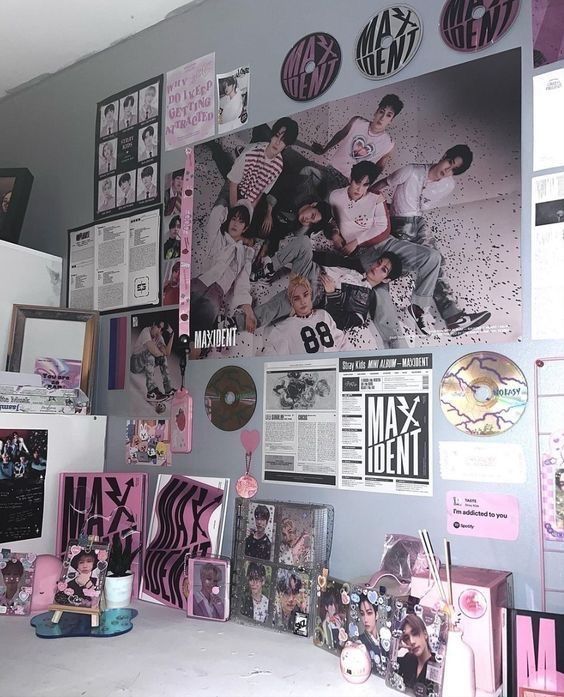 a wall covered in posters and pictures next to a desk with a cup on it