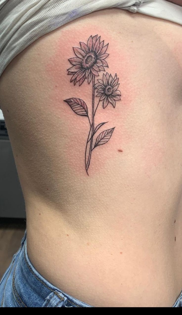 a sunflower tattoo on the back of a woman's rib - up stomach