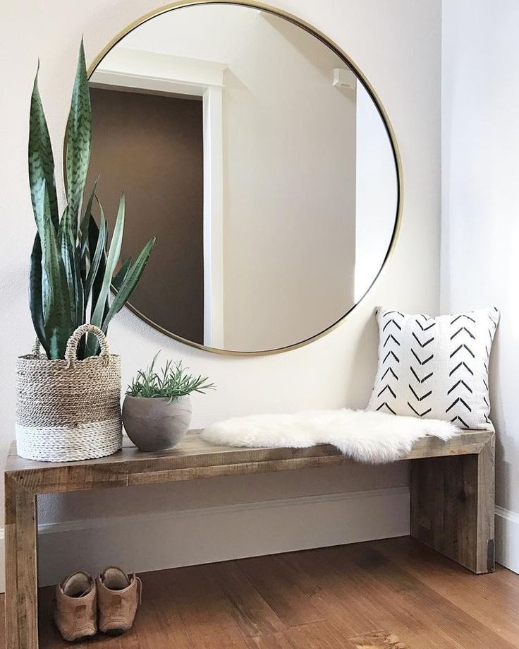 a wooden bench sitting under a round mirror next to a potted plant on top of a hard wood floor