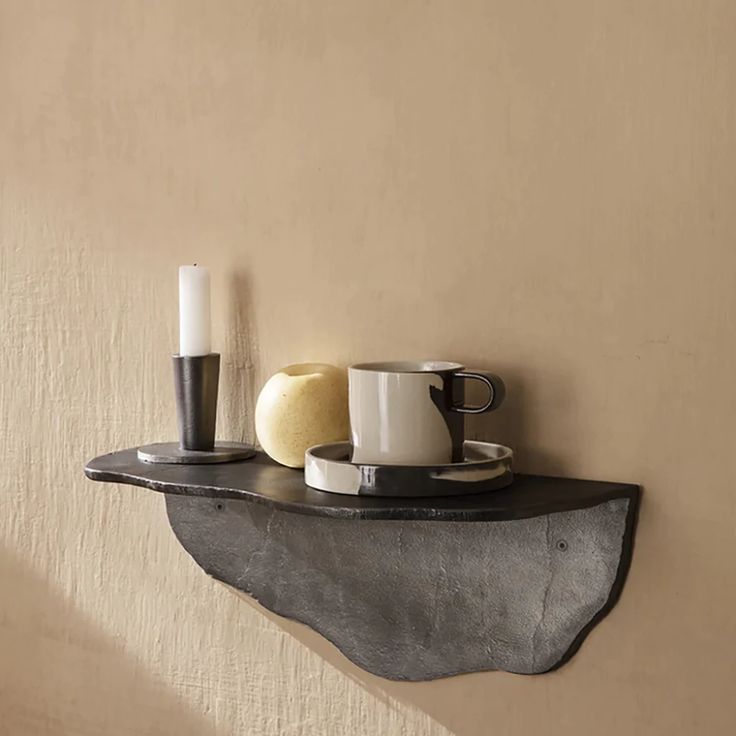 a shelf with two mugs on it and a candle in the corner next to it