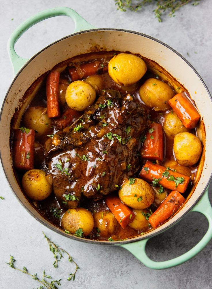 pot roast with carrots, potatoes and gravy in a green dutch oven