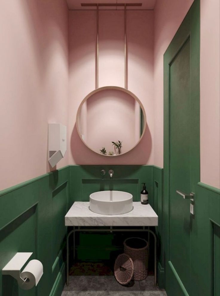 a pink and green bathroom with a round mirror above the sink, toilet paper roll holder on the wall