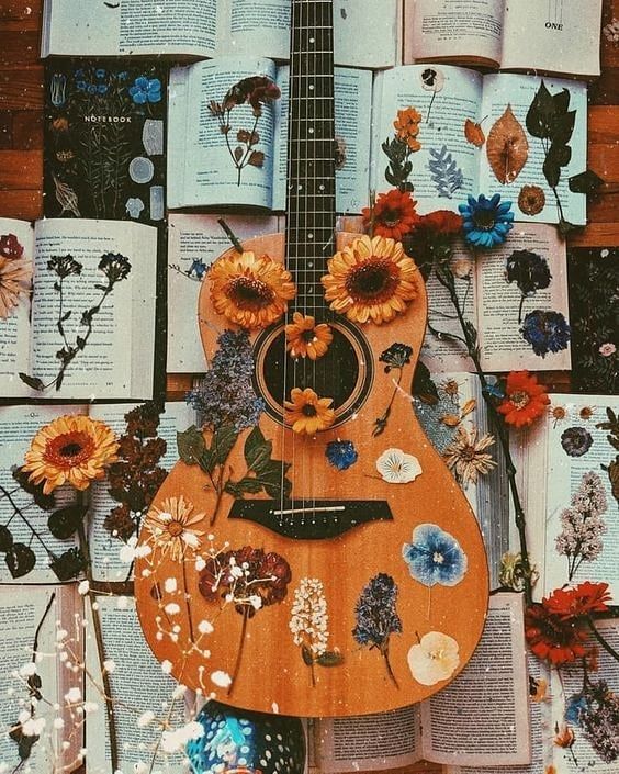 an acoustic guitar surrounded by books and flowers