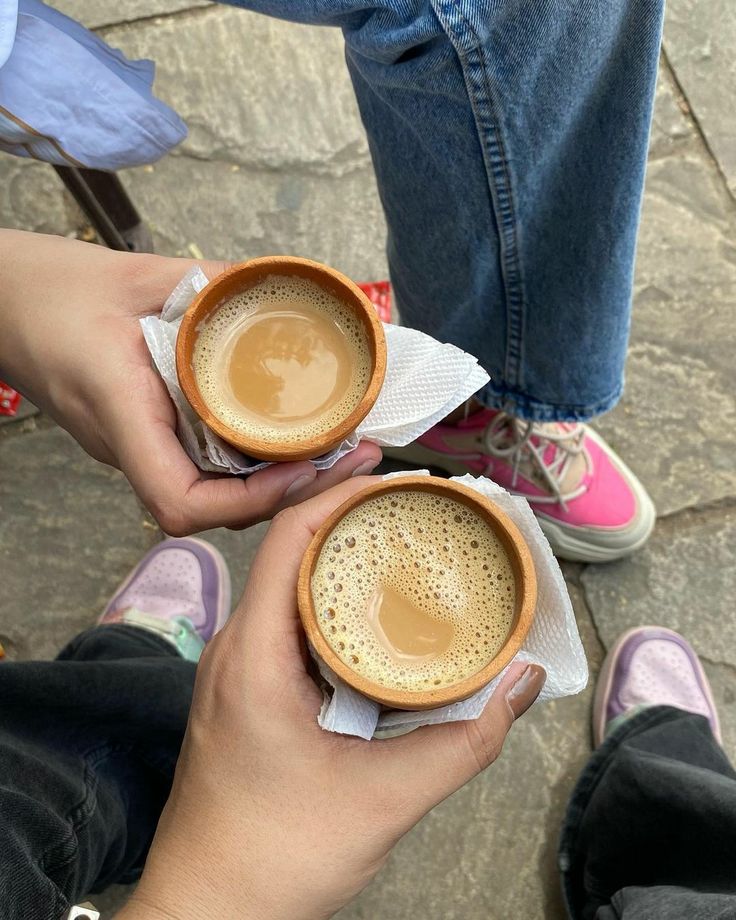 two people holding cups of coffee on top of napkins in their hands, with one person's legs crossed