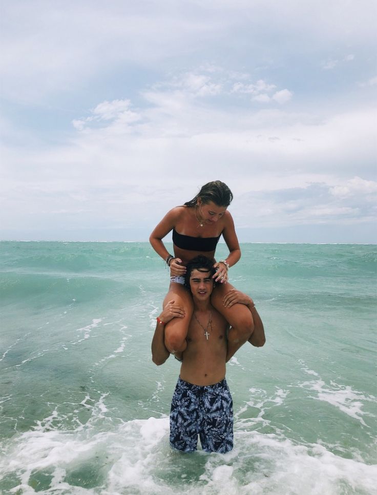 two people standing in the ocean with one person on his shoulders and another man holding an infant