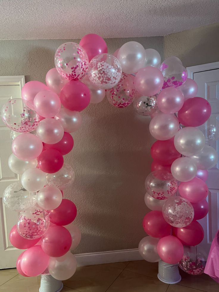 a pink and white balloon arch with lots of balloons on it's sides in front of a door