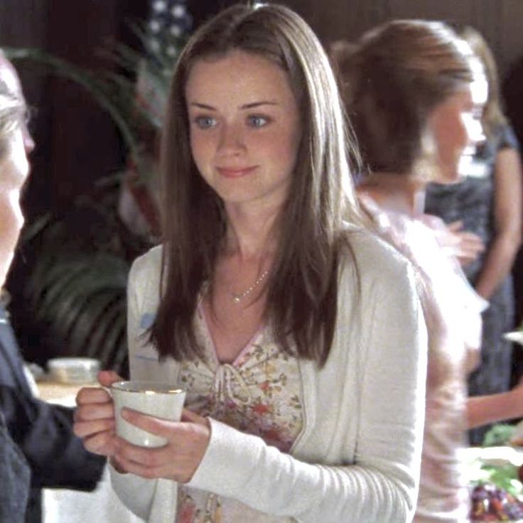 a woman holding a cup in her hand and talking to another person at a table