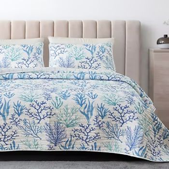 a bed with blue and white corals on the comforter, pillows and headboard