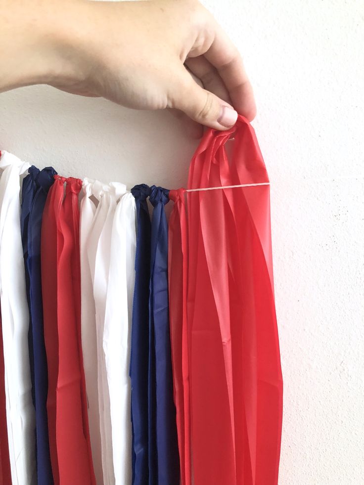 someone is holding up some red, white and blue ribbons in front of a wall