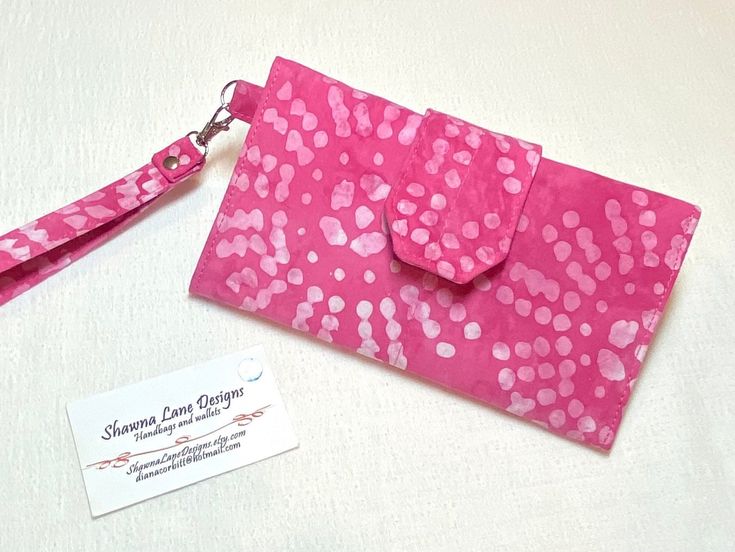 "This wallet with wristlet strap is made from a colorful pink batik fabric. It is the perfect cell phone accessory that will hold all of your credit cards and checkbook! Get organized with this pretty, trifold style wallet!  The wallet with detachable wrist strap that you see in the first several pictures is what you are purchasing, it's ready to ship now!  (Last picture is sample wallet showing the many things this wallet will hold!) Dimensions: Approx. size is 7 ¾\" wide X 4 ½\" tall when closed. Wallet is approx. 13 ½\" X 7 ¾\" when fully opened up.  cell phone pocket  7 3/4\" wide x 4\" tall Detachable Wrist strap including metal hardware is approx. 7 1/2\" long x 5/8\" wide. This multi-functional wallet provides a place for your checkbook and register, has a pen holder, 6 credit card Pink Trifold Wallet With Card Slots As Gift, Cheap Pink Wallets With Card Slots, Pink Bifold Wallet For Daily Use, Pink Bifold Wallet With Card Slots, Pink Rectangular Wallet With Card Slots, Perfect Cell, Purse Hardware, Credit Card Wallet, Trifold Wallet