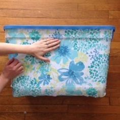 two hands are holding onto a blue and white flowered bag on a wooden floor