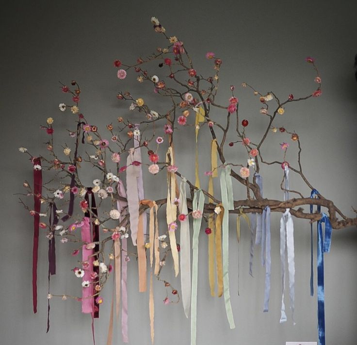 an art piece with ribbons hanging from it's branches and flowers on the wall