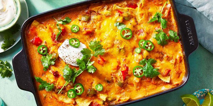 an enchilada casserole with sour cream and cilantro on the side