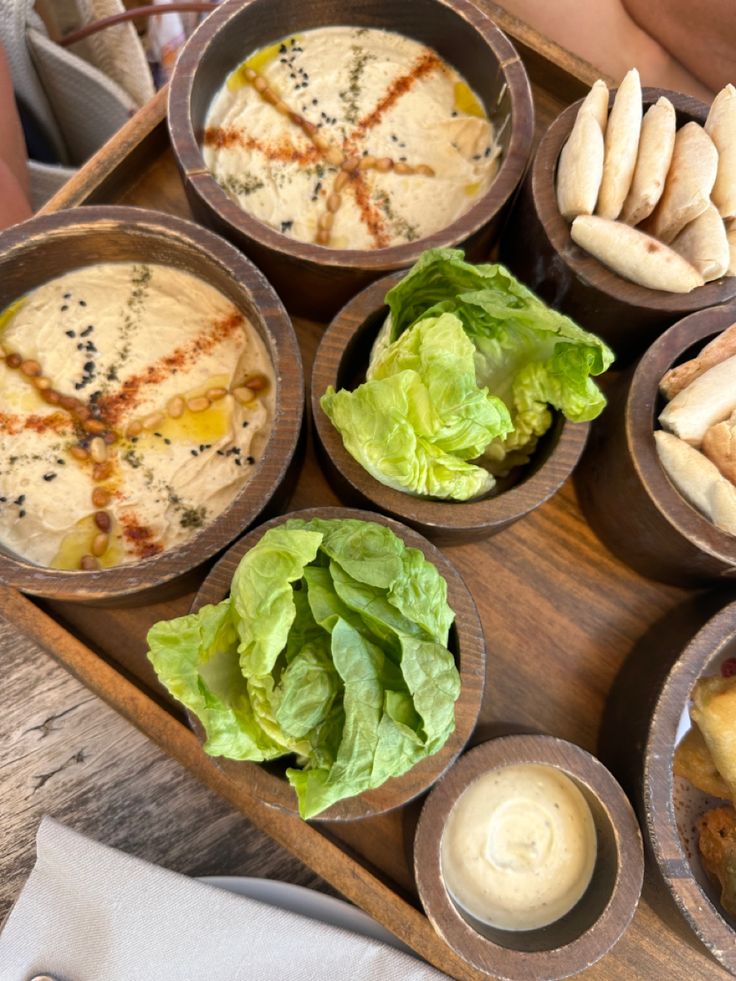 a wooden tray topped with different types of food next to dipping sauces and condiments