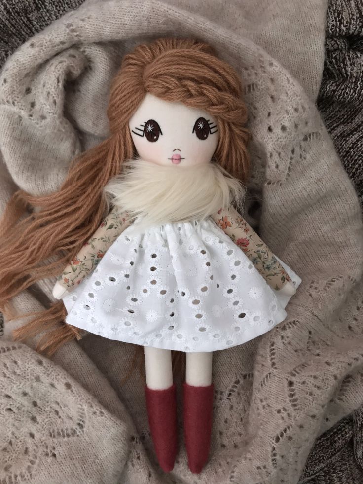 a doll with long red hair and brown eyes laying on top of a white blanket