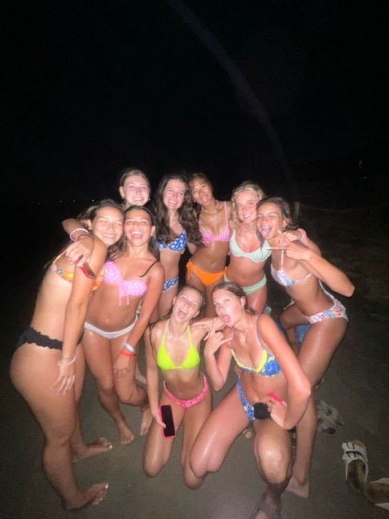 a group of women in bikinis posing for a photo on the beach at night