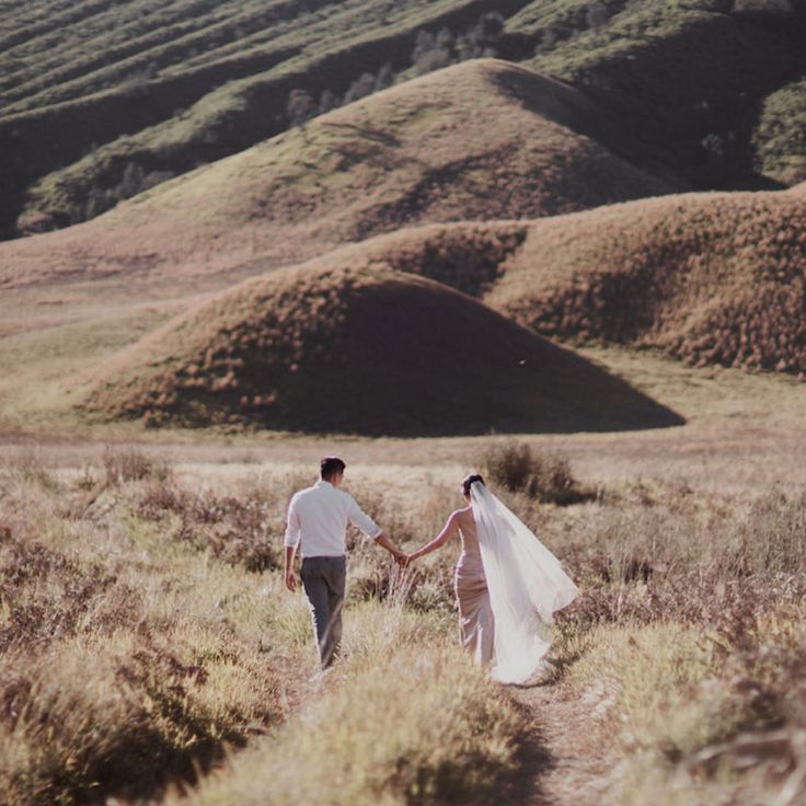 a bride and groom walking in the mountains holding hands