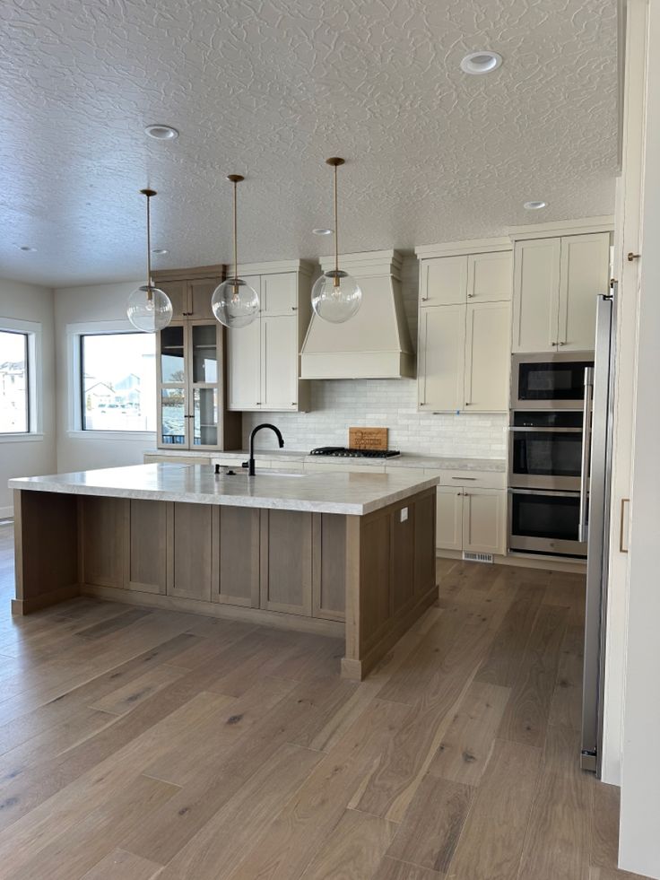 a large kitchen with an island in the middle and two lights hanging from the ceiling