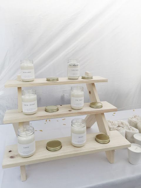 three tiered shelf with jars and candles on it in front of a white backdrop