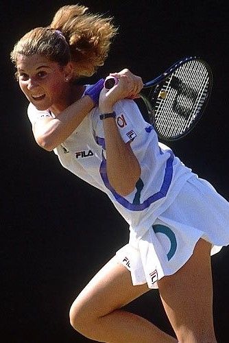 a female tennis player is swinging her racket to hit the ball with both hands