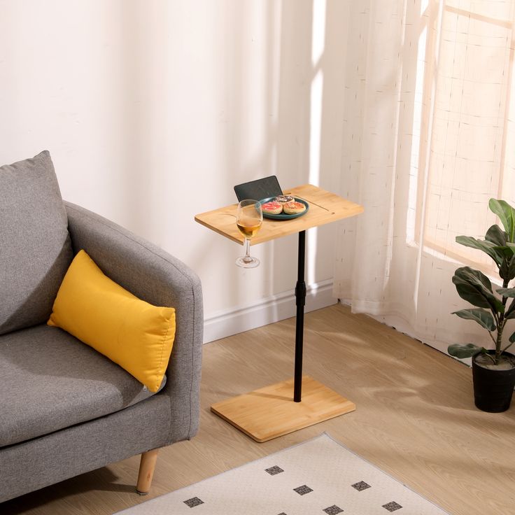 a small table with a laptop on it next to a gray couch and potted plant