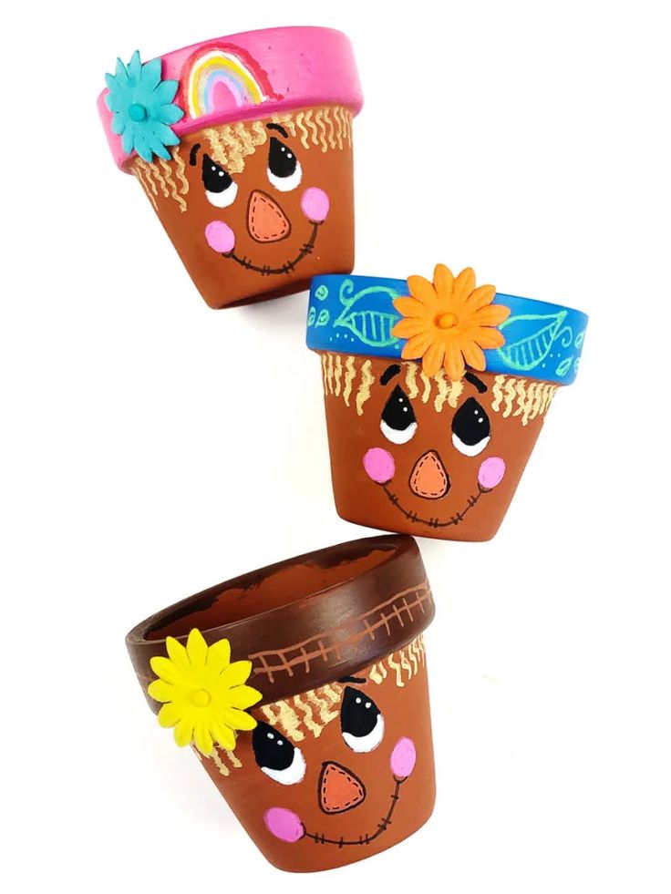 three pots with faces painted on them and one has a flower in its hair, the other has a sunflower