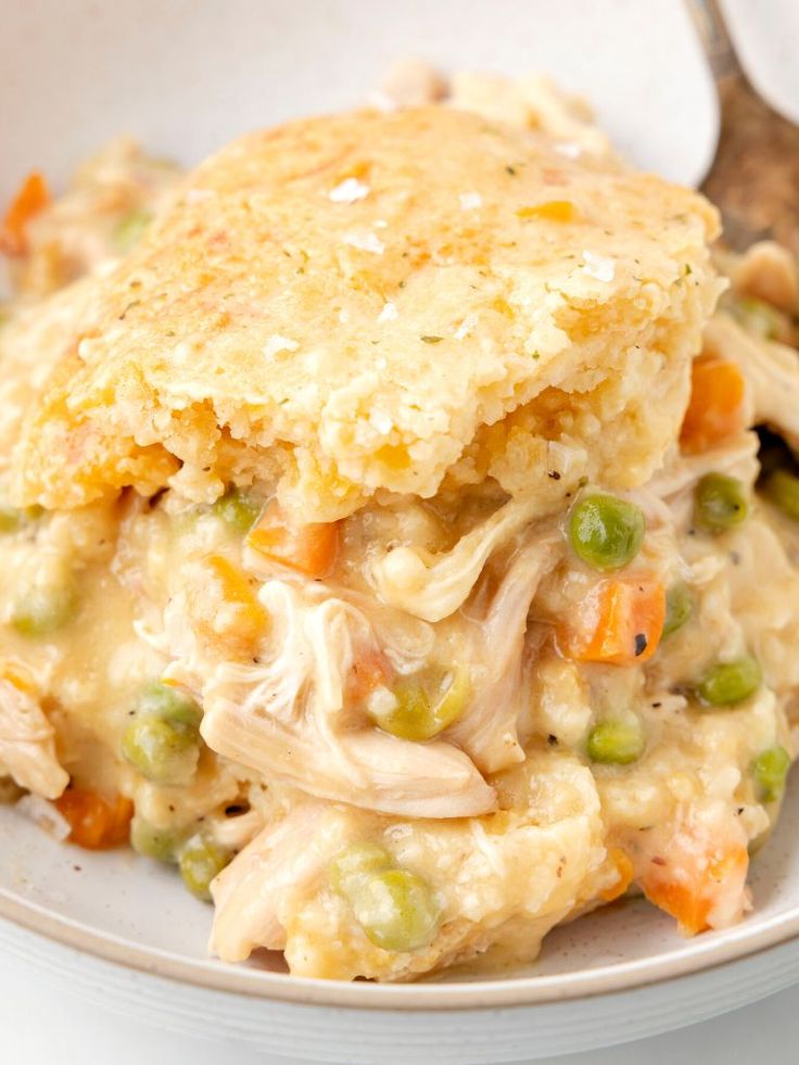 a white bowl filled with chicken pot pie and vegetables next to a fork on the side