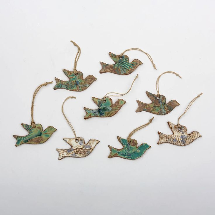 six metal birds hanging from strings on a white surface with green and gold accents,