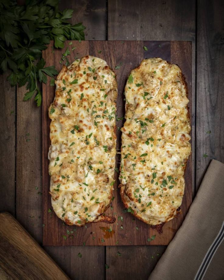 two pieces of bread covered in cheese on a wooden cutting board next to a knife