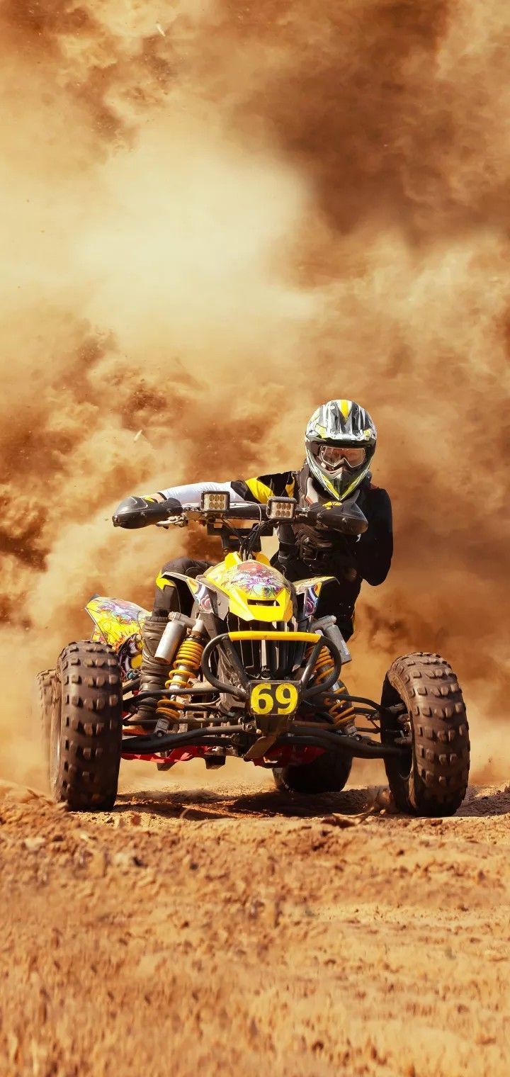 a man riding on the back of a yellow four - wheeled vehicle in dirt field