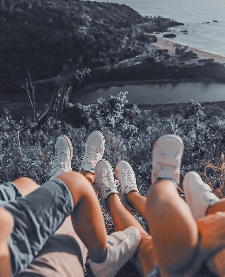 two people sitting on the ground with their feet up looking out at water and land