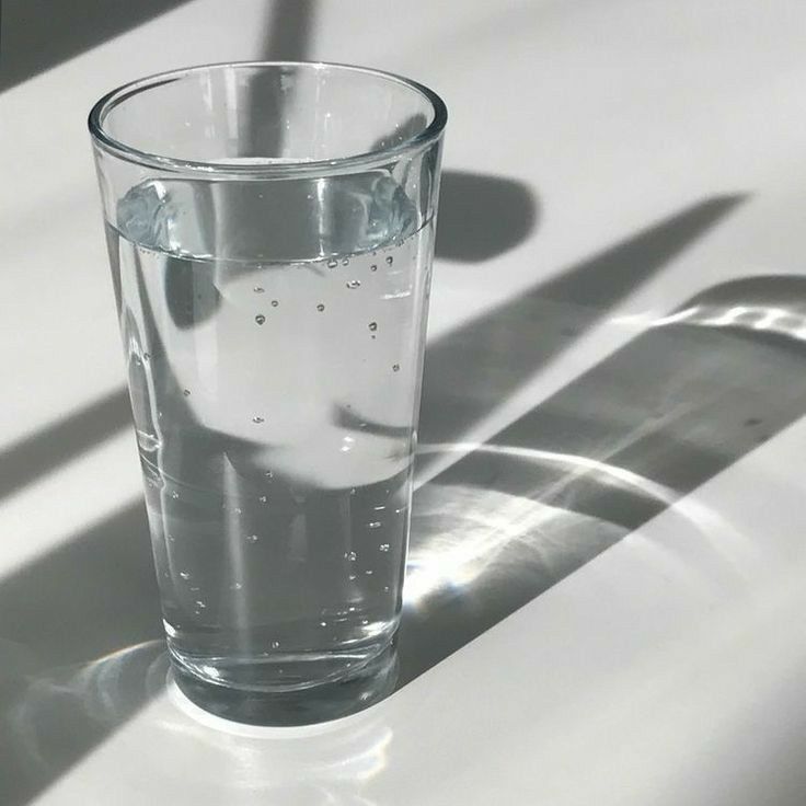 a glass filled with water sitting on top of a white table next to a shadow