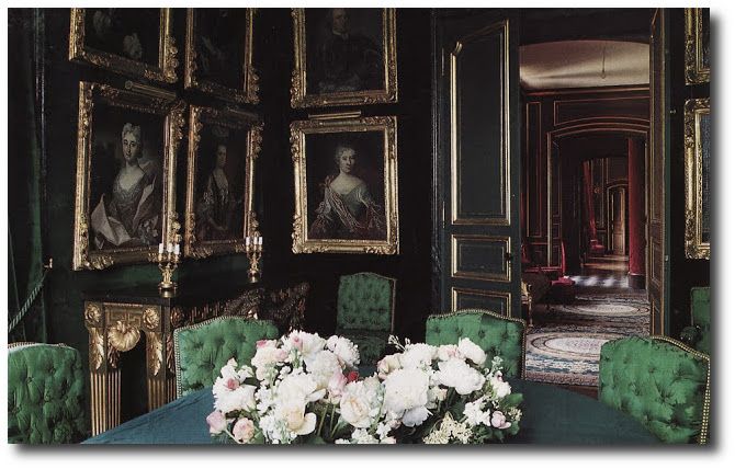 a dining room with green velvet chairs and pictures on the wall above it, along with white flowers in a vase