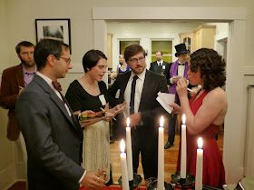 a group of people standing around a cake with lit candles on it and one person holding a piece of paper