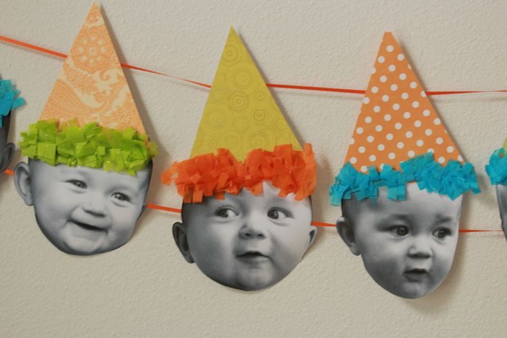 three babys wearing party hats hanging on a line with orange and blue streamers