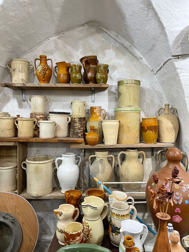 many vases and bowls are on shelves in a room with an arched doorway that leads into the kitchen