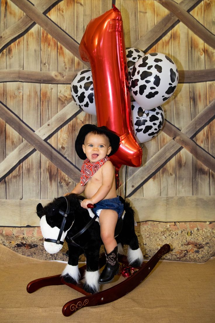 a small child sitting on top of a rocking horse with balloons in the shape of a number one