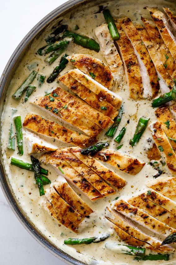 a pan filled with chicken and asparagus covered in white sauce