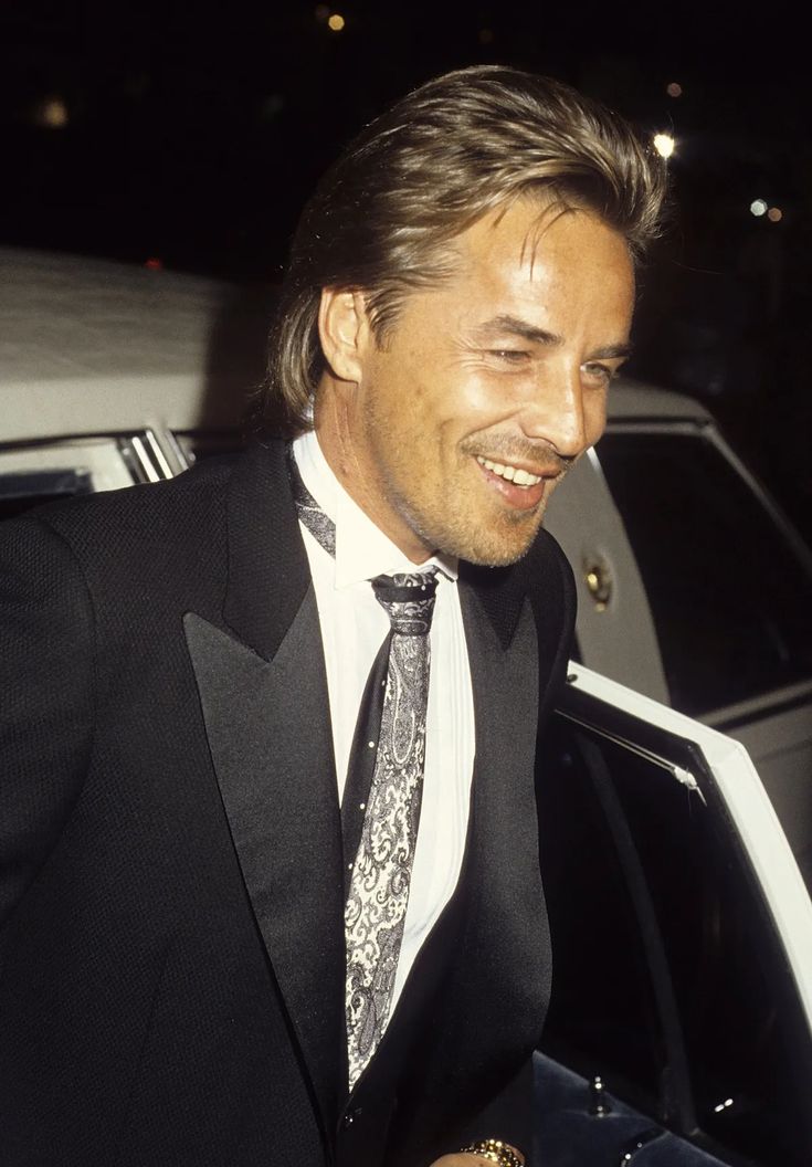 a man in a tuxedo smiles as he walks out of a car at night