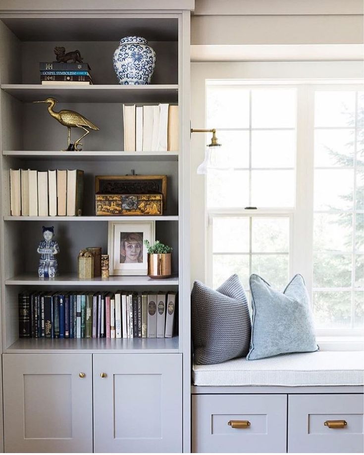 a window seat in the corner of a room with bookshelves and pillows on it