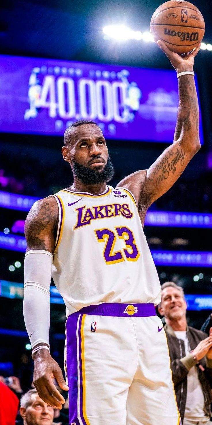 a man holding a basketball in his right hand while standing on a court with other people watching