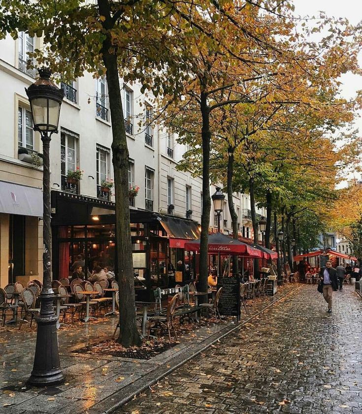 people are walking down the cobblestone street in an old european city with many tables and chairs