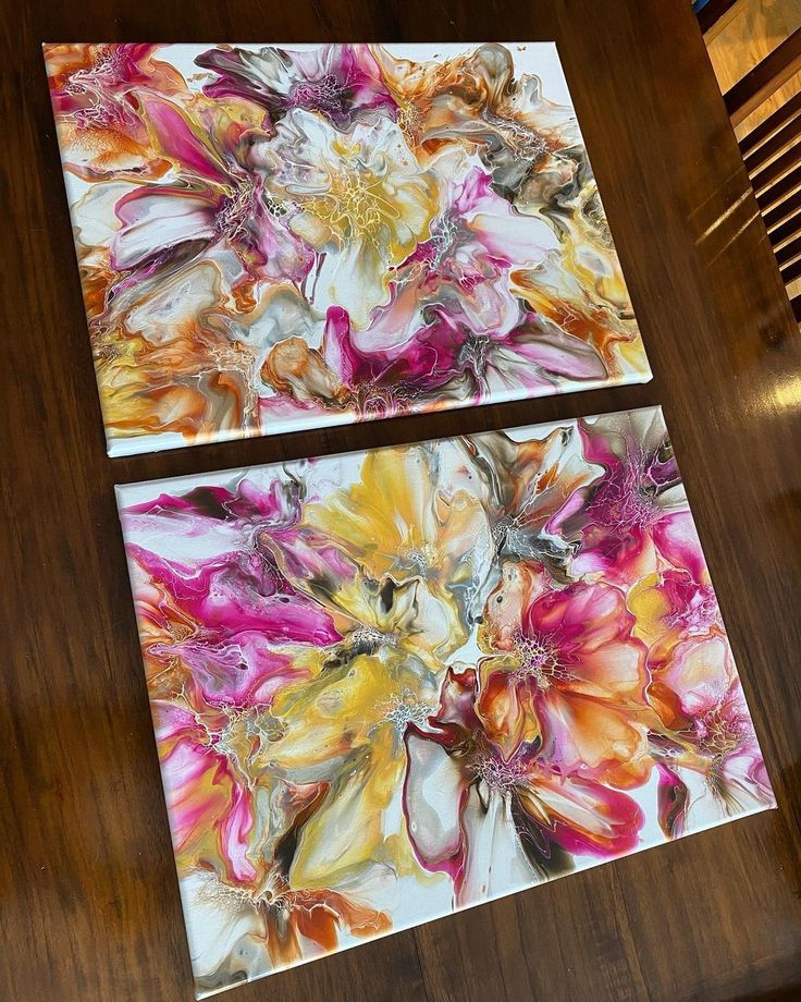 two square paintings on a wooden table in the shape of flowers, each with different colors and shapes