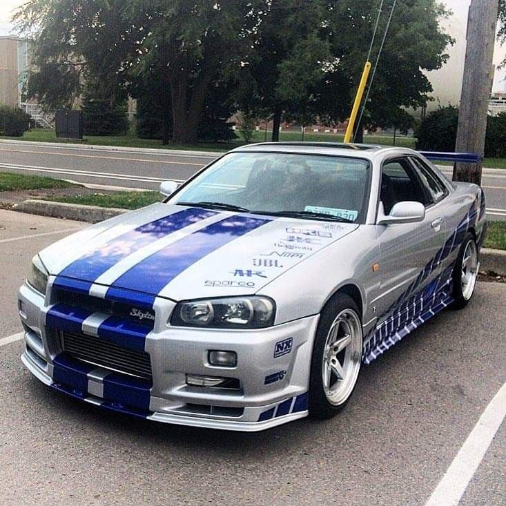 a silver and blue car parked in a parking lot next to a street with trees