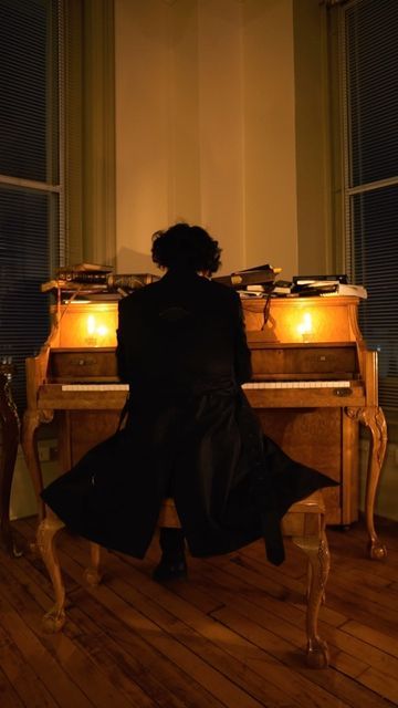 a woman sitting at a piano in front of a window with candles on the table